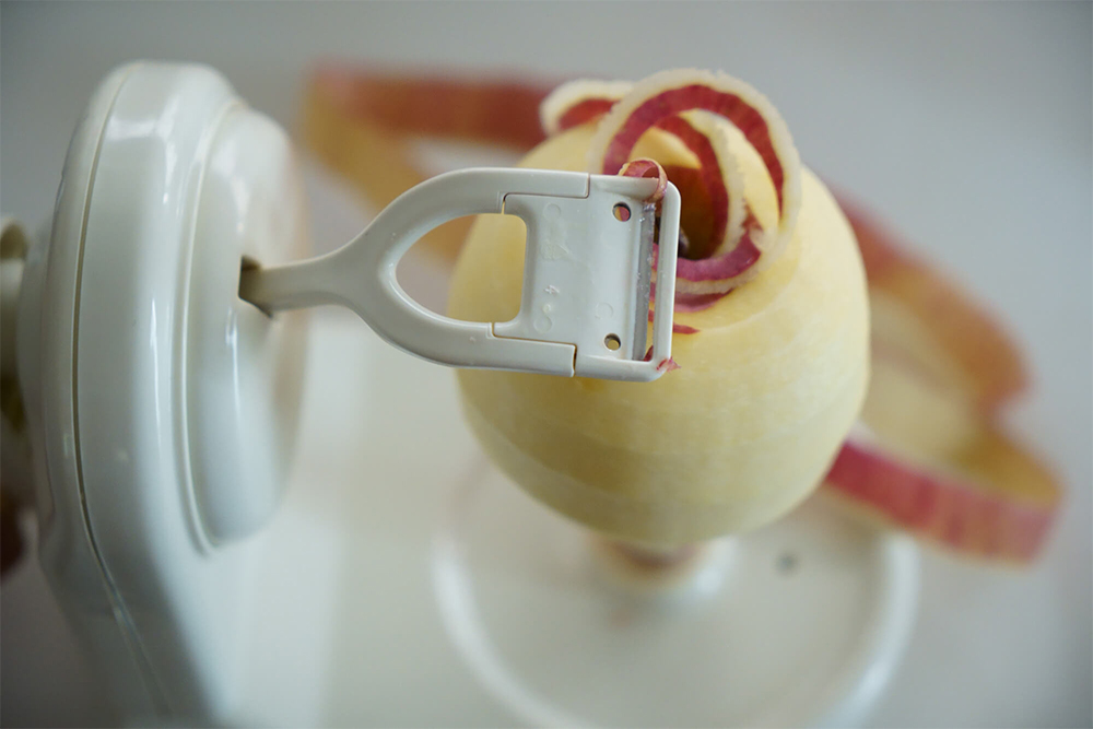 アップルピーラーの刺しピンにリンゴの下部中央を真っ直ぐに刺して、ハンドルを回す。 リンゴが回転すると同時に刃の付いたアームが動いて皮が剥ける。リンゴのサイズは直径8～9㎝が望ましい。 まな板に移して、包丁で縦半分に切ってから、くし形4～5等分に。芯を包丁で押し切りにした後、一口大にカット。