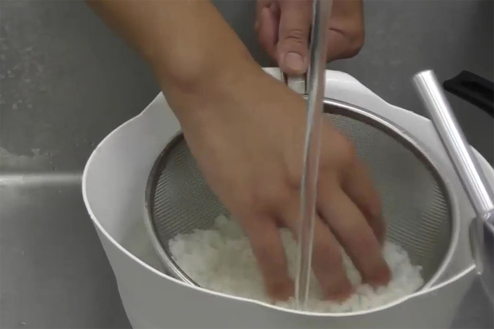 茹でた米をザルにあげ、流水が直接米に当たらないよう、ボウルに水をためながらやさしくほぐすように洗う。