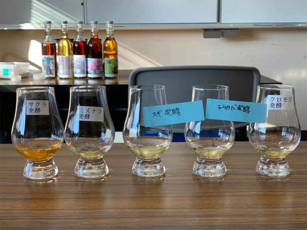 （2020年12月鹿山さんのFacebookより）森林総合研究所で香りのテイスティング。左からサクラ、ミズナラ、スギ、シラカバ、クロモジの木の蒸溜酒。