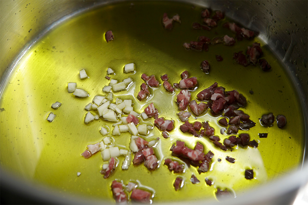 鍋にオリーブ油を熱し、ニンニク、生ハムを弱火で香りが出るまで炒める。生ハムは硬いので細かめに刻む。