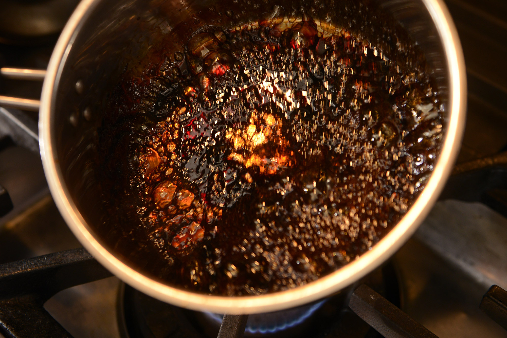 【６】濃い焦げ茶色に色づいたら熱湯75mlを２回に分けて加える。余熱でどんどん火が入り、鍋底に飴状に固まるので、熱を当てて溶かすようさらに火を入れる。 POINT：「常識外れだろ！」と言われるほど黒くなるまで、カラメルを焦がす。お酒にも合う味作りの秘訣。