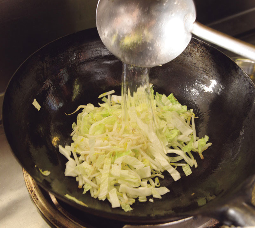 [７]白菜、キャベツを加える 白菜とキャベツを合わせたものをひとつかみ加え、鶏ガラスープ50ml、塩小さじ１弱を加えて炒める。