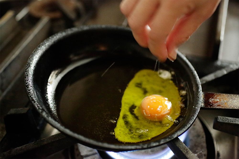 [２]卵を割り落とす トングなどで軽くつまんで、ニンニクが柔らかくなったのを確認したら取り出し、フライパンを傾け、卵を割り落とす。 POINT：油の温度はそれほど高くないので、最初、卵は油の中に静かに沈む状態。