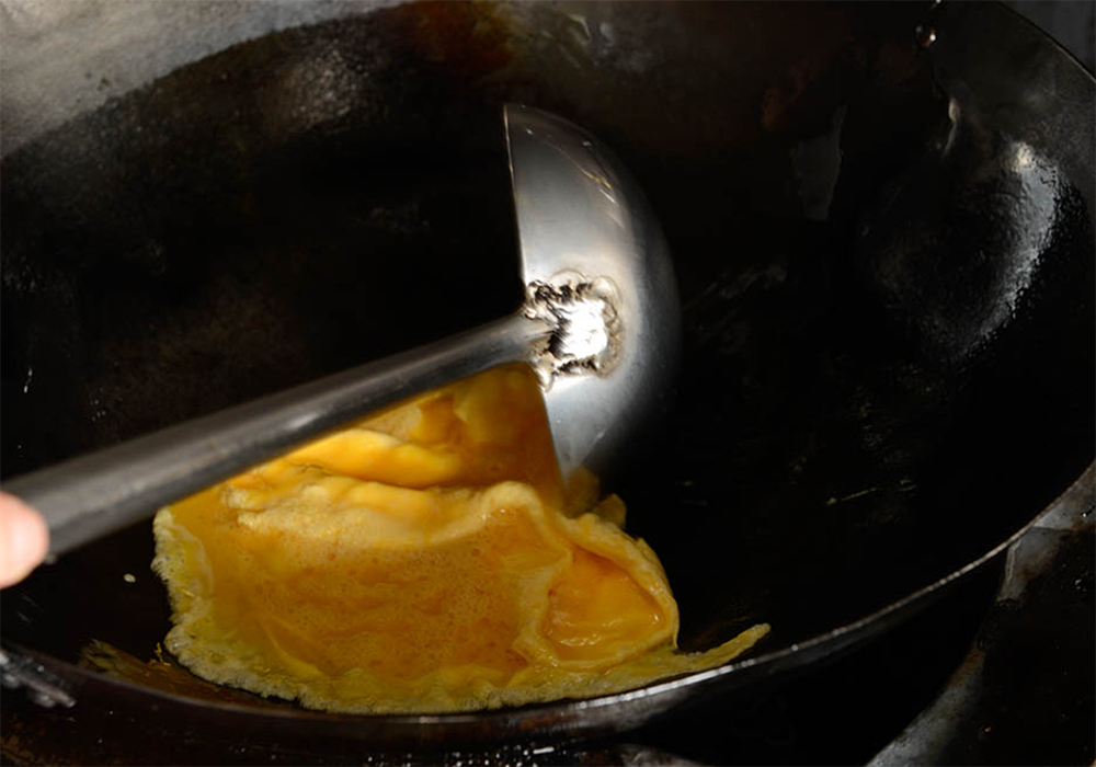 [５]卵を内側に返す 中華鍋の真ん中にゆっくり落としていく。火を中火に上げ、卵の周りが固まってきたら、外側から内側に向かって卵を返す。