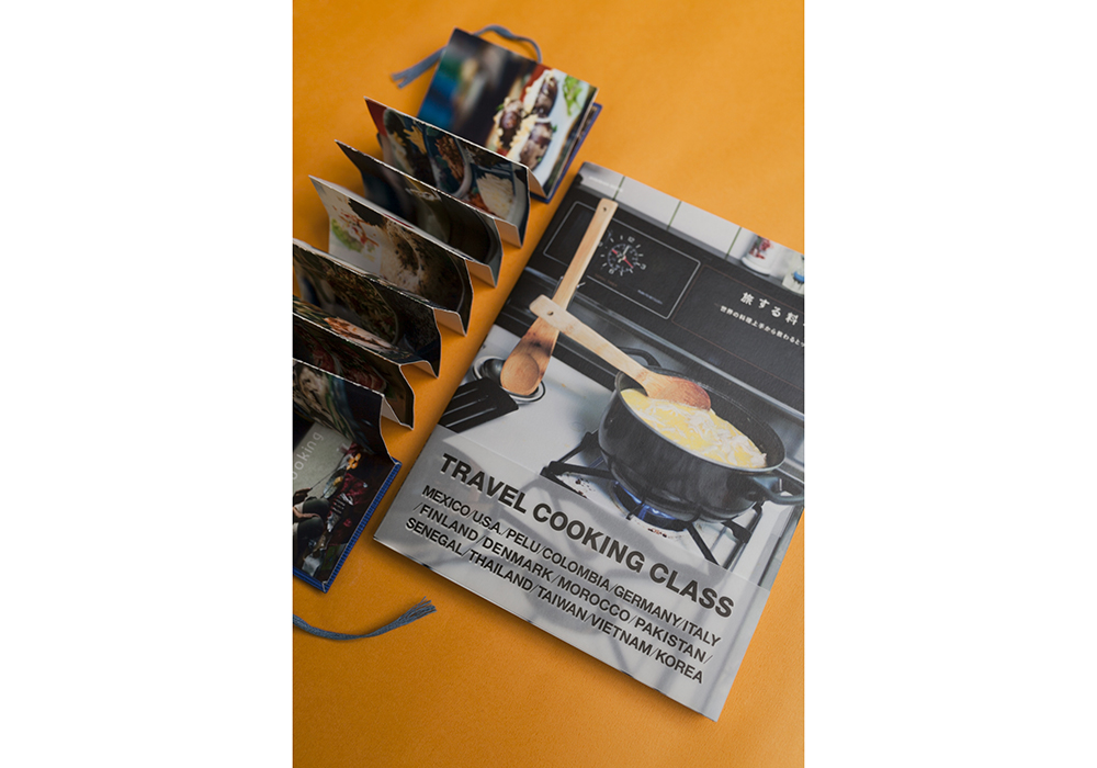 世界の料理写真が載った、手作りのじゃばら型冊子（左上）。教室の内容を説明するのに用いる。料理教室の先生たちのレシピは書籍としても紹介された（右）。