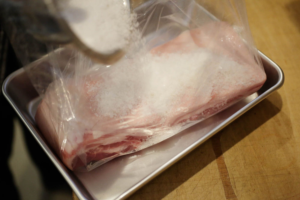 ビニール袋に肉を入れて、塩を２、３回に分けて加える。 [２]塩で肉を覆う
