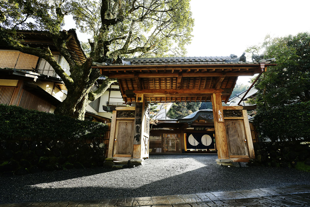 修善寺の山門で宿坊として開業した歴史を物語る堂々たる門構え。春には桜と新緑、夏は青葉、秋は紅葉と、四季折々の自然が遠来の客人を迎え入れる。