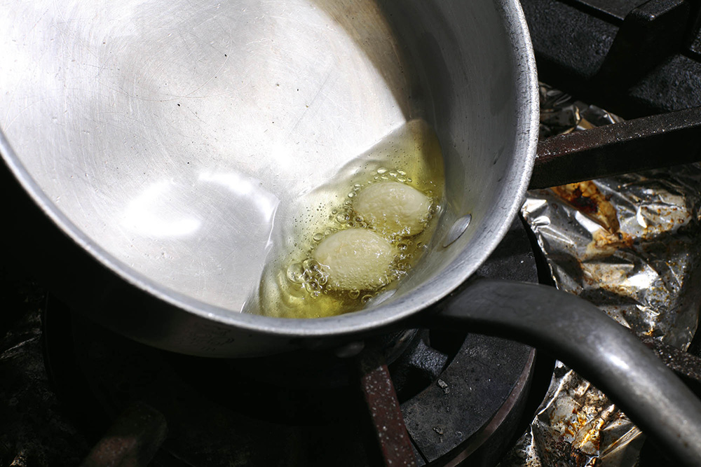 たっぷりめのオリーブ油を鍋で熱し、つぶしたニンニクを炒める