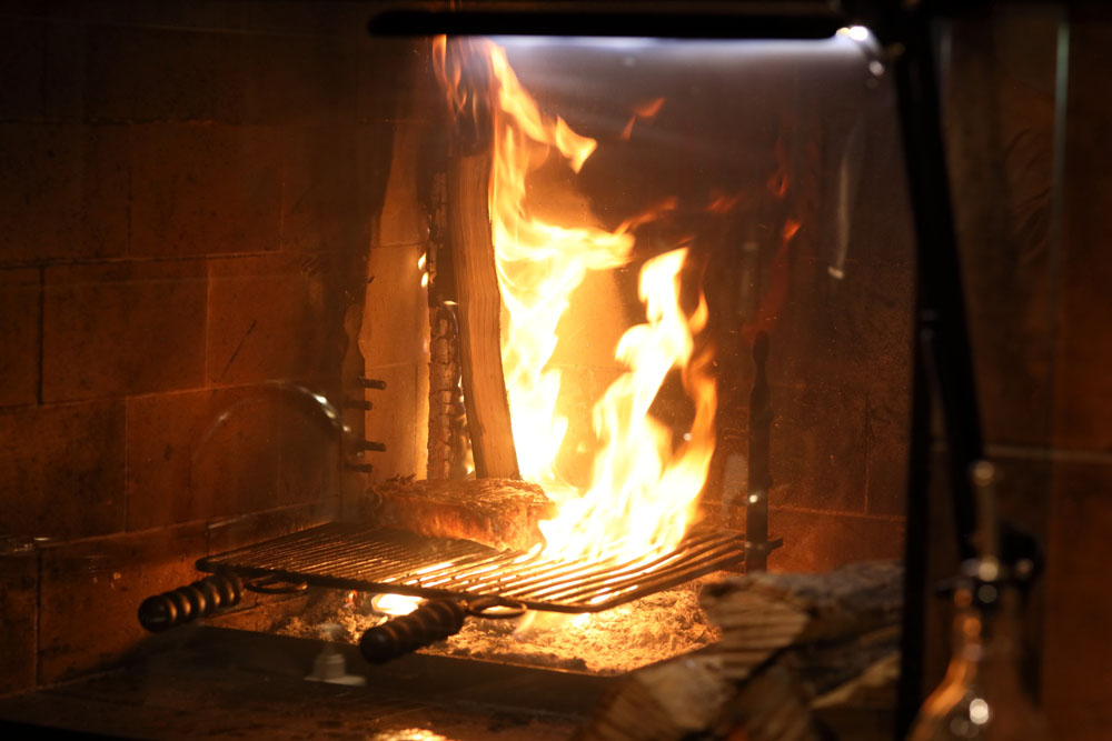 肉を熾火で焼き始める。写真の炎は奥で燃やす薪が上げているもの。肉には直接当てない。扉を閉めた状態なので、炎が上に上がっている。