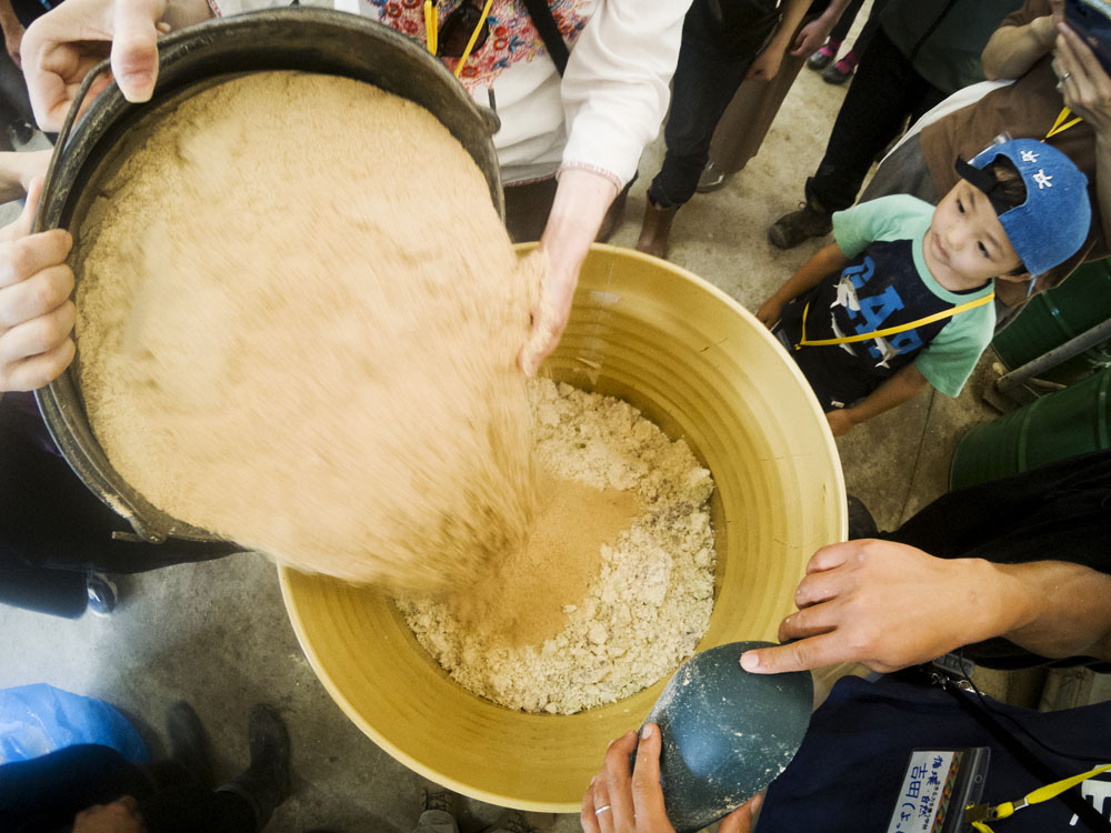 嫌気性発酵飼料作りを体験。おからと米ぬかを交互に混ぜてドラム缶に７層ほど重ねていきます。