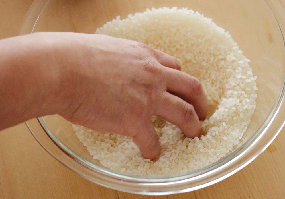 ボウルに米を入れ、指先を回して優しく混ぜる。少量の水を加えてさらに混ぜる。