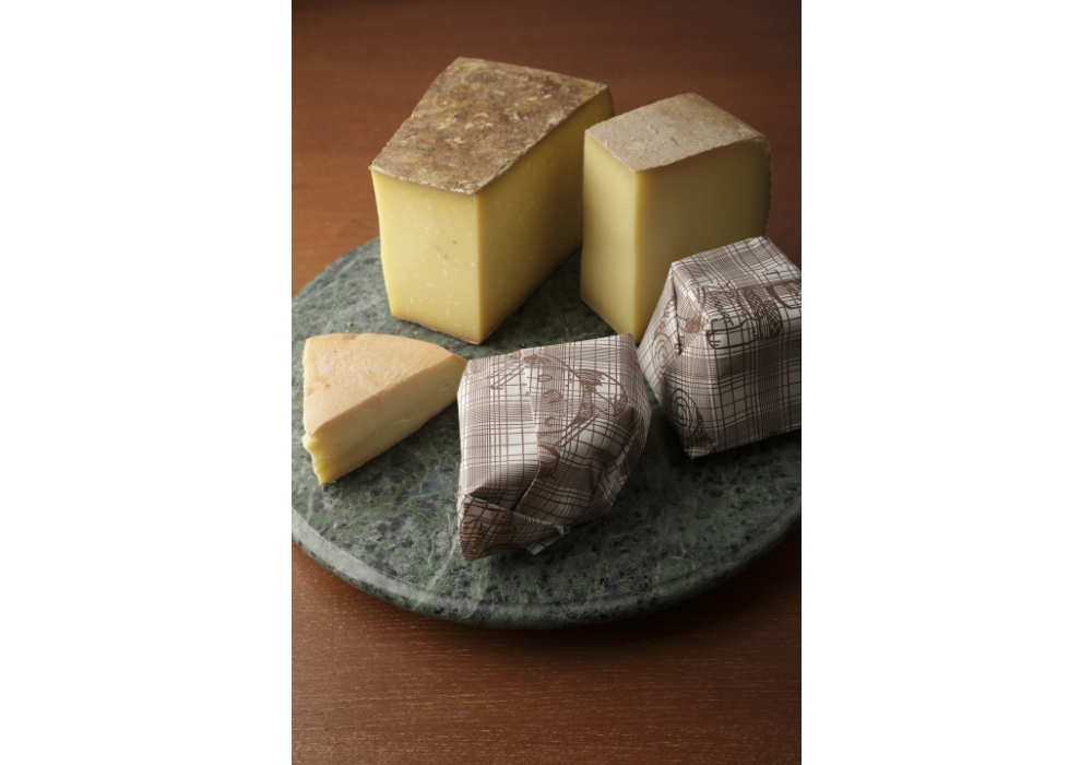 フランスのチーズ店では、チーズの包装も学んだ。テープを使わずにまとめる。「菓子屋包みに似ていますが、折りの方向などが違うんです」。手前の包装紙はシェーブル（山羊）専用のもの。奥はコンテ、手前のウォッシュはアベイ・ド・シトー。