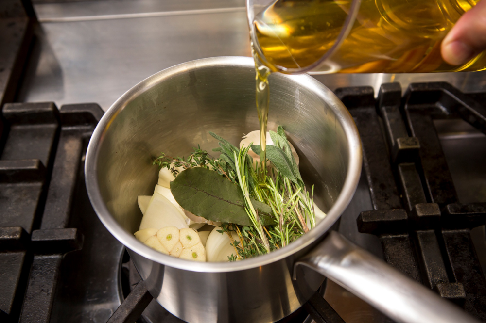 オーリオ・プロフマートを作る。タマネギ、ニンニク、ローズマリー、セージ、タイム、ローリエを鍋に入れ、オリーブ油を注ぐ。